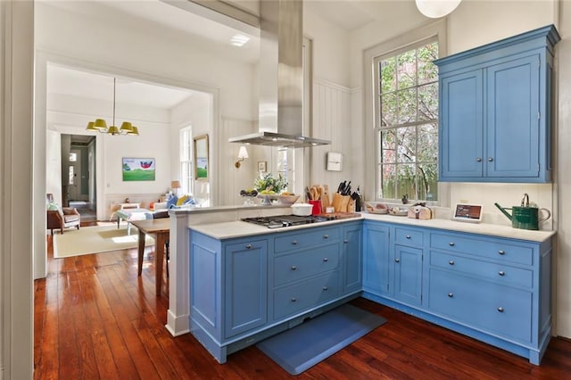 kitchen with stainless steel gas cooktop, a peninsula, dark wood finished floors, island exhaust hood, and blue cabinetry