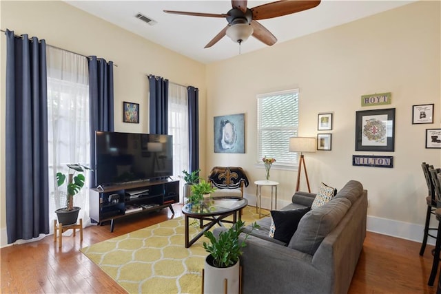 living area featuring baseboards, visible vents, ceiling fan, and wood-type flooring