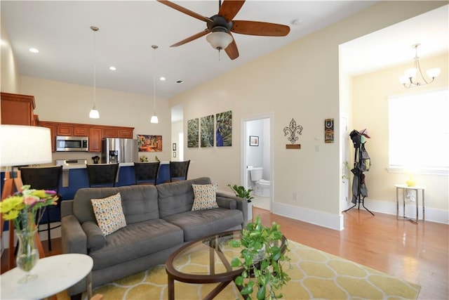 living room with light wood finished floors, ceiling fan with notable chandelier, recessed lighting, and baseboards