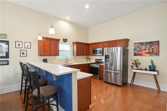 kitchen with light countertops, a sink, a breakfast bar area, appliances with stainless steel finishes, and a peninsula