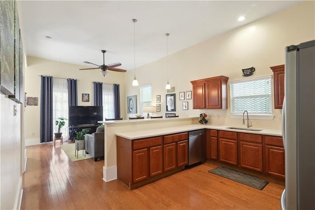 kitchen with a sink, light wood finished floors, appliances with stainless steel finishes, a peninsula, and open floor plan
