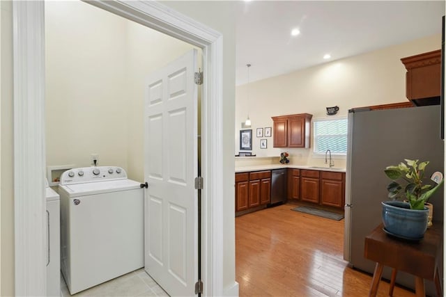 laundry area with washing machine and dryer, a sink, light wood finished floors, laundry area, and recessed lighting
