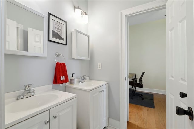 bathroom with baseboards, a sink, two vanities, and wood finished floors