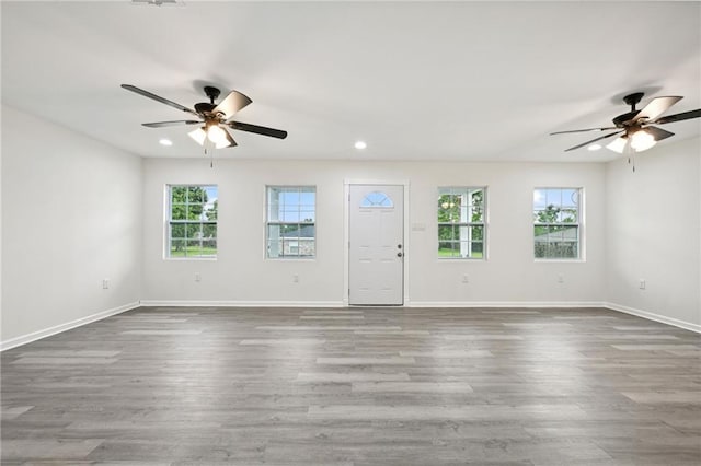 unfurnished living room with plenty of natural light, baseboards, wood finished floors, and a ceiling fan