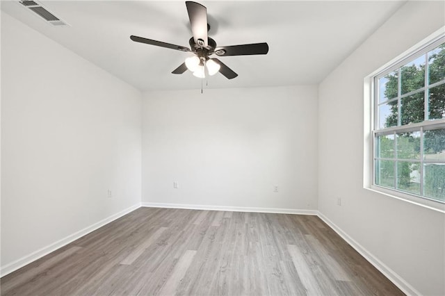 empty room featuring baseboards, visible vents, plenty of natural light, and wood finished floors