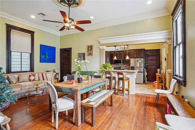 dining area featuring light wood-style flooring, crown molding, ceiling fan, and visible vents