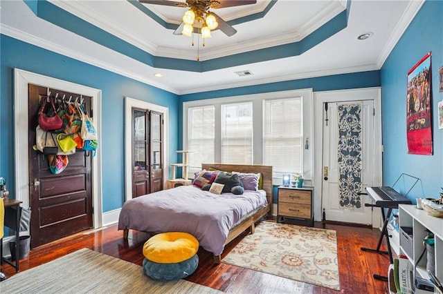 bedroom with visible vents, a tray ceiling, crown molding, and wood finished floors