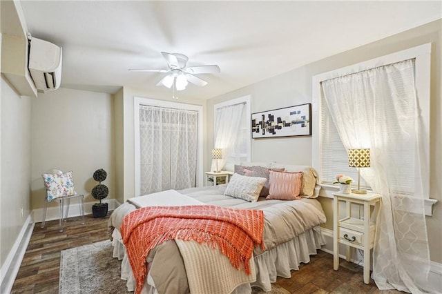 bedroom with a ceiling fan, an AC wall unit, baseboards, and wood finished floors