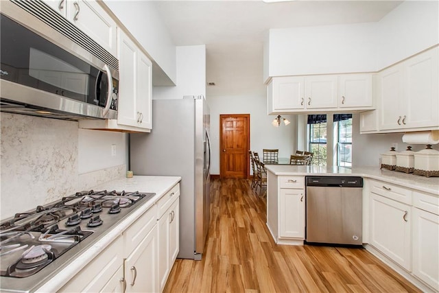 132 Country Club Dr, Covington, LA 70433 - kitchen with light countertops, light wood-style flooring, white cabinets, tasteful backsplash, and appliances with stainless steel finishes