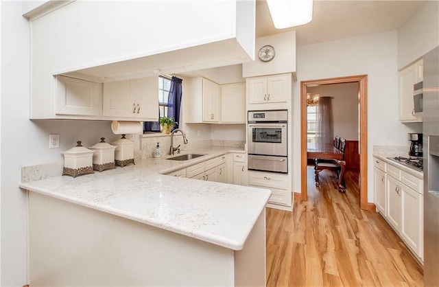 132 Country Club Dr, Covington, LA 70433 - kitchen with a sink, a warming drawer, appliances with stainless steel finishes, a peninsula, and light wood-type flooring