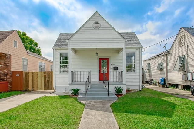 view of front of home featuring covered porch, fence, roof with shingles, and a front lawn