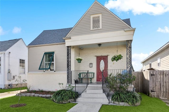 4718 Annette St, New Orleans, LA 70122 - view of front facade featuring fence, a front yard, covered porch, brick siding, and a shingled roof