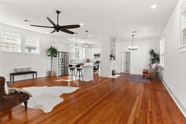 living room featuring dark wood-style flooring, recessed lighting, visible vents, and ceiling fan with notable chandelier
