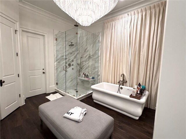 bathroom with a stall shower, a notable chandelier, wood finished floors, a soaking tub, and ornamental molding