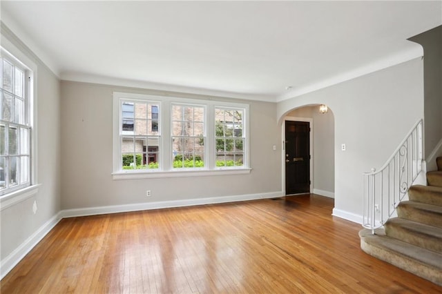 unfurnished living room with arched walkways, baseboards, light wood finished floors, and stairs