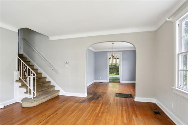 spare room featuring wood finished floors, arched walkways, baseboards, a notable chandelier, and visible vents