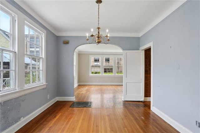 unfurnished dining area featuring arched walkways, a chandelier, baseboards, and hardwood / wood-style flooring
