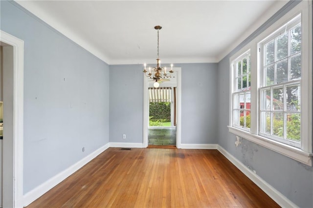 empty room featuring visible vents, hardwood / wood-style flooring, baseboards, and an inviting chandelier