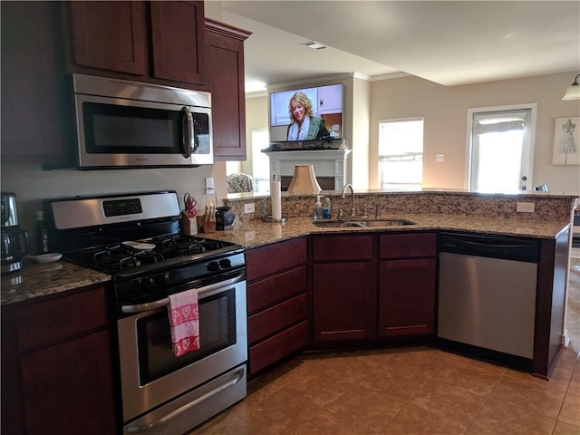 kitchen featuring dark tile patterned flooring, a peninsula, stone counters, appliances with stainless steel finishes, and a sink