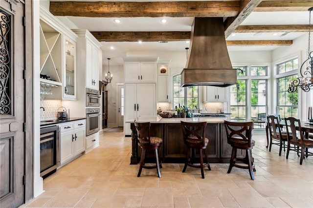 kitchen featuring a chandelier, a breakfast bar, beverage cooler, island range hood, and white cabinets