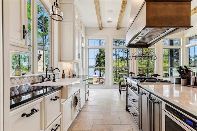kitchen featuring custom exhaust hood, light stone countertops, tasteful backsplash, a sink, and stone tile floors