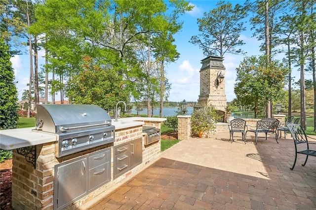 view of patio / terrace with a grill, exterior kitchen, a water view, and an outdoor fireplace