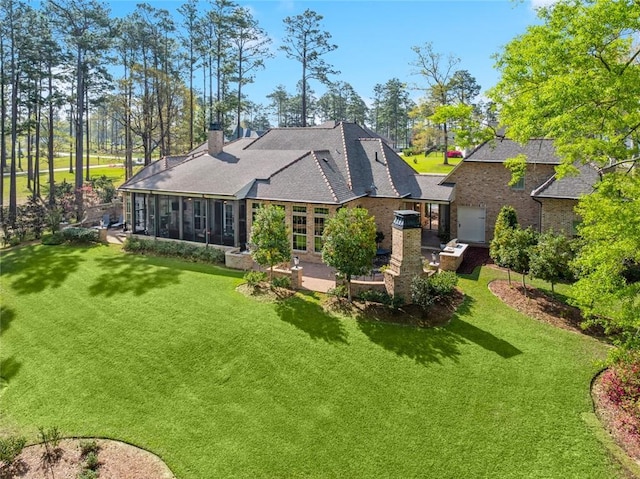 back of house featuring a sunroom, a chimney, brick siding, a lawn, and a shingled roof