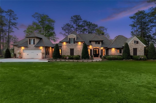 french country home featuring a lawn, driveway, and brick siding