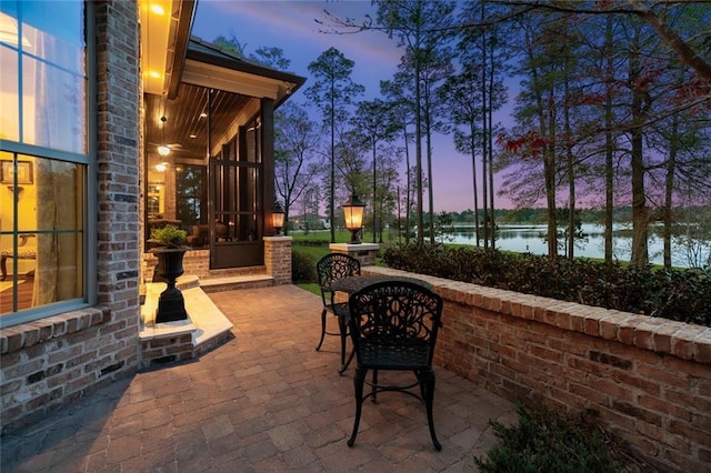patio terrace at dusk featuring a water view and a sunroom
