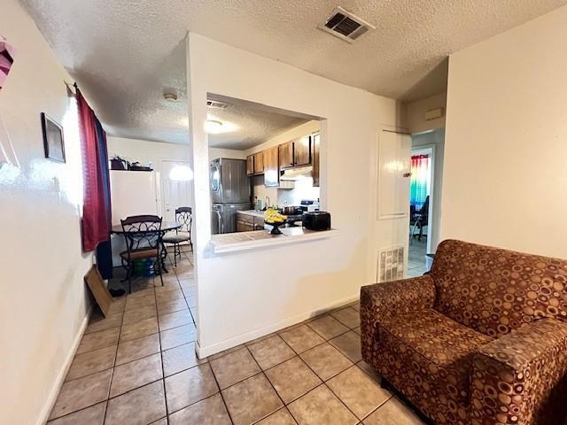 kitchen featuring freestanding refrigerator, a textured ceiling, visible vents, and light tile patterned floors