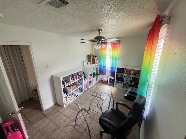 interior space with tile patterned flooring, ceiling fan, a textured ceiling, and visible vents