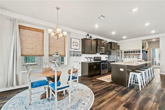 405 Short Bough Ln, Slidell, LA 70461 - kitchen featuring appliances with stainless steel finishes, ornamental molding, a chandelier, a kitchen bar, and dark wood finished floors