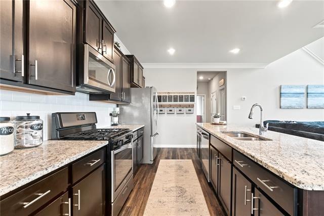 405 Short Bough Ln, Slidell, LA 70461 - kitchen with stainless steel appliances, dark wood-style floors, dark brown cabinets, light stone countertops, and crown molding