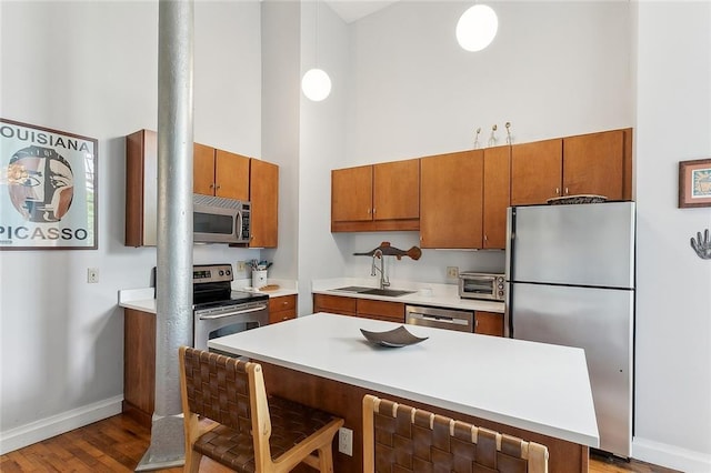 kitchen with a towering ceiling, baseboards, brown cabinets, a sink, and appliances with stainless steel finishes