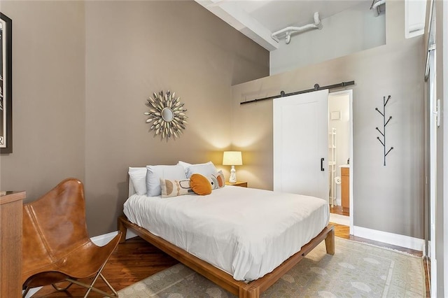 bedroom featuring baseboards, ensuite bathroom, light wood finished floors, and a barn door