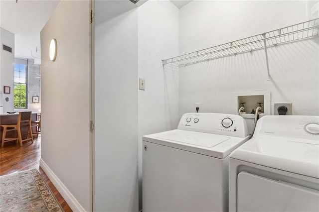 clothes washing area featuring separate washer and dryer, baseboards, wood finished floors, and visible vents