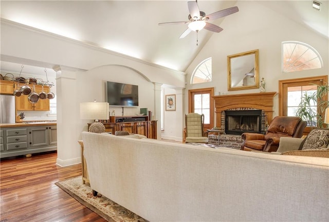 living room with a ceiling fan, wood finished floors, a brick fireplace, and plenty of natural light