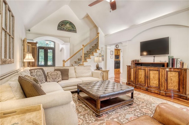 living room with arched walkways, a ceiling fan, stairway, and light wood-type flooring