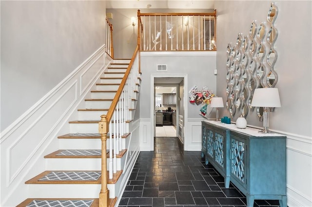 1100 Vintage Dr, Kenner, LA 70065 - stairs featuring a wainscoted wall, a high ceiling, a decorative wall, stone tile flooring, and visible vents