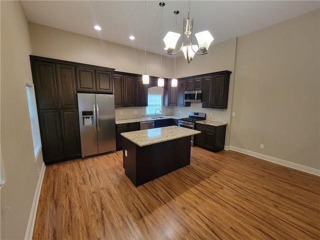 kitchen with a notable chandelier, light wood-type flooring, stainless steel appliances, a kitchen island, and dark brown cabinetry