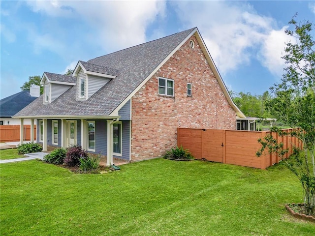 view of side of property with covered porch, a lawn, fence, brick siding, and roof with shingles
