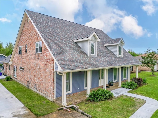 view of front facade with roof with shingles, a porch, brick siding, and a front lawn