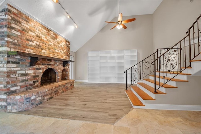 unfurnished living room with baseboards, ceiling fan, a fireplace, rail lighting, and high vaulted ceiling
