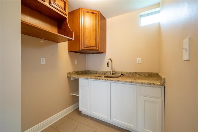 kitchen with white cabinets, light tile patterned floors, a sink, and baseboards