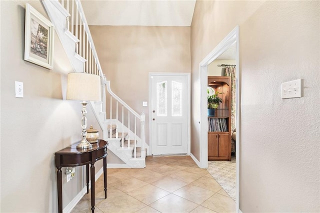 tiled foyer with baseboards, a high ceiling, and stairs