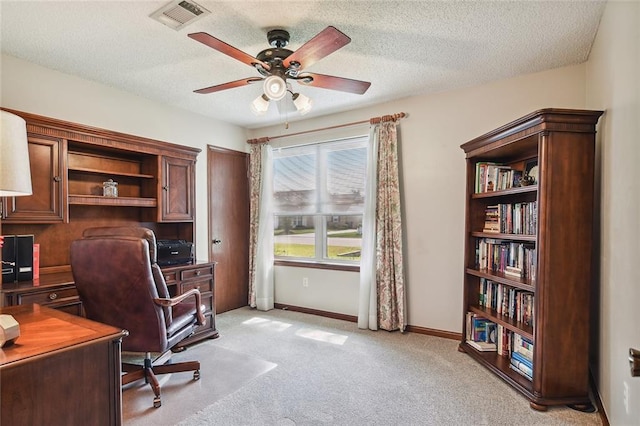 office area with a textured ceiling, visible vents, ceiling fan, light carpet, and baseboards