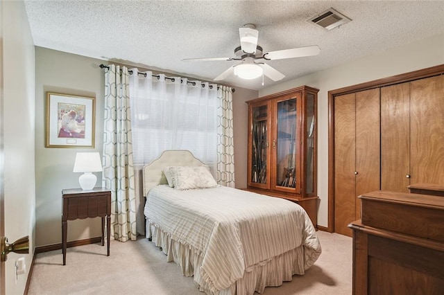 bedroom featuring a closet, a textured ceiling, ceiling fan, visible vents, and light carpet