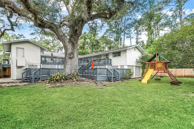 back of property with a lawn, fence, a wooden deck, and a playground