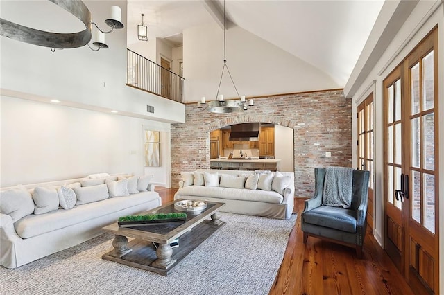 living room featuring arched walkways, high vaulted ceiling, wood finished floors, and brick wall