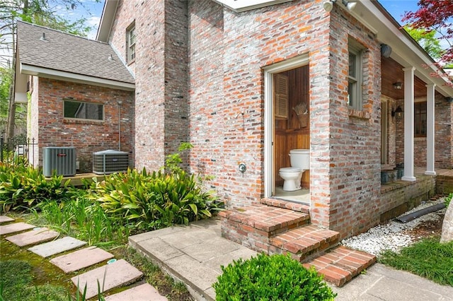 entrance to property featuring central air condition unit, covered porch, and brick siding